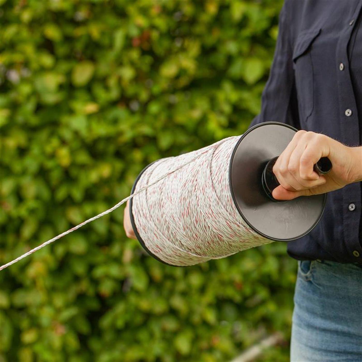 Person håller i en 400 m VOSS.farming trådrulle för betesstängsel med praktisk dispenser; tyska: med praktisk dispenser. inkl. 10 kontaktdon &amp; varningsskylt, 3x 0,25 koppar + 3x 0,20 rostfritt stål, set om 5 trådrullar.